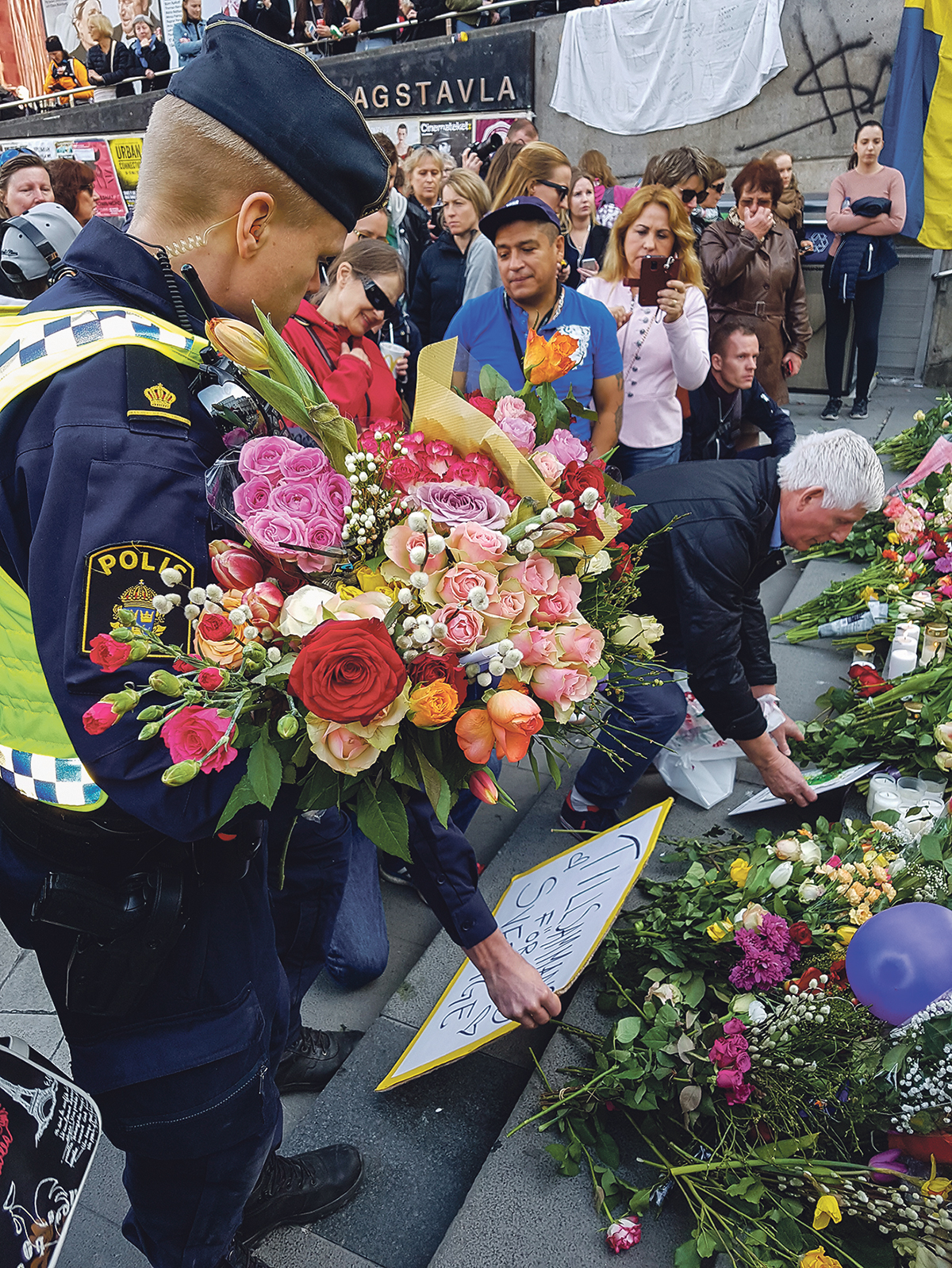 En polis har samlat ihop blommor  som människor prytt Polisens bilar med, och lägger dem på trappan vid Sergels torg i Stockholm.