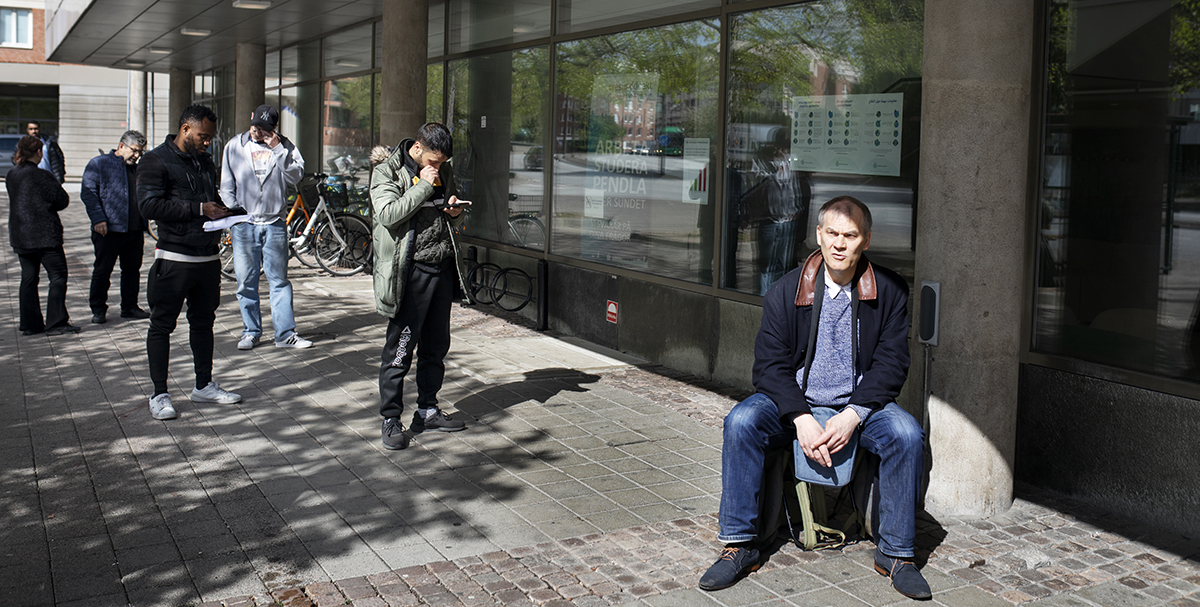 När kundtorget öppnar är kön redan lång. En man tar numera med egen stol, eftersom kundtorgets stolar tagits bort som en pandemiåtgärd.