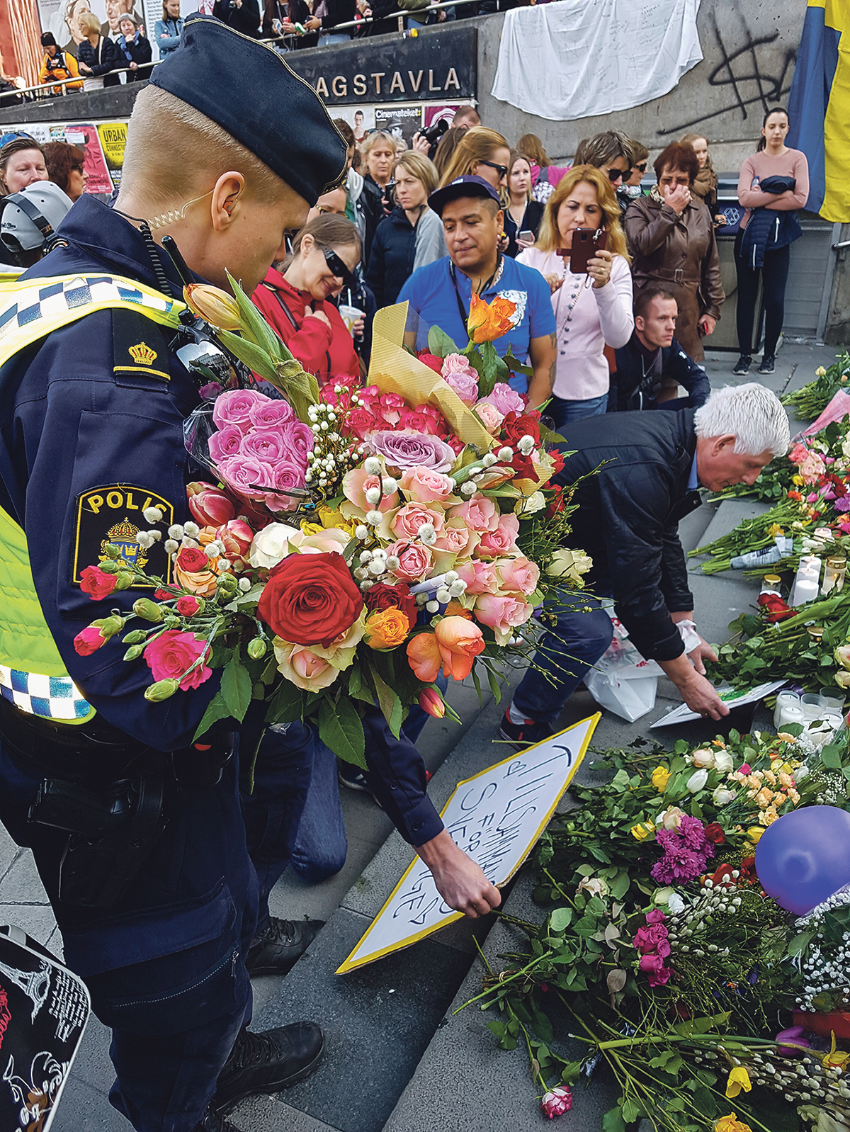 En polis har samlat ihop blommor som människor prytt Polisens bilar med, och lägger dem på trappan vid Sergels torg i Stockholm.